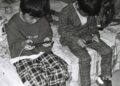 Twee jongens zitten op een bed en kijken allebei naar hun smartphone