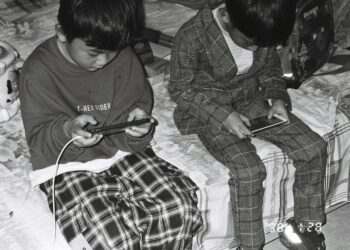 Twee jongens zitten op een bed en kijken allebei naar hun smartphone