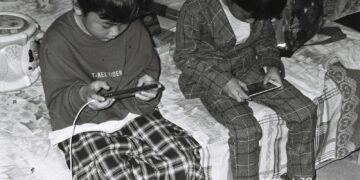 Twee jongens zitten op een bed en kijken allebei naar hun smartphone