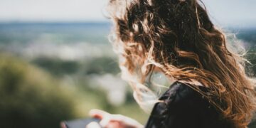 Jonge vrouw met lang krullend haar kijkt op haar smartphone